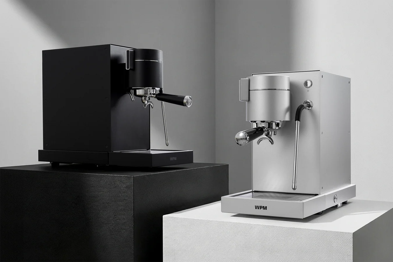 Two WPM PRIMUS espresso machines, one black and one silver, on a neutral background.