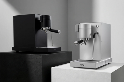 Two WPM PRIMUS espresso machines, one black and one silver, on a neutral background.